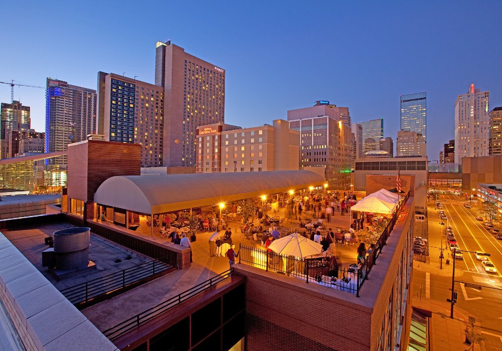 The Denver Athletic Club at dusk with the downtown Denver skyline behind it