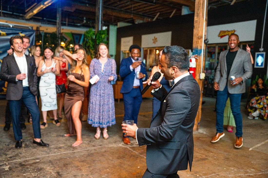A host singing into a microphone as guests dance at the 3rd Annual Fall Ball
