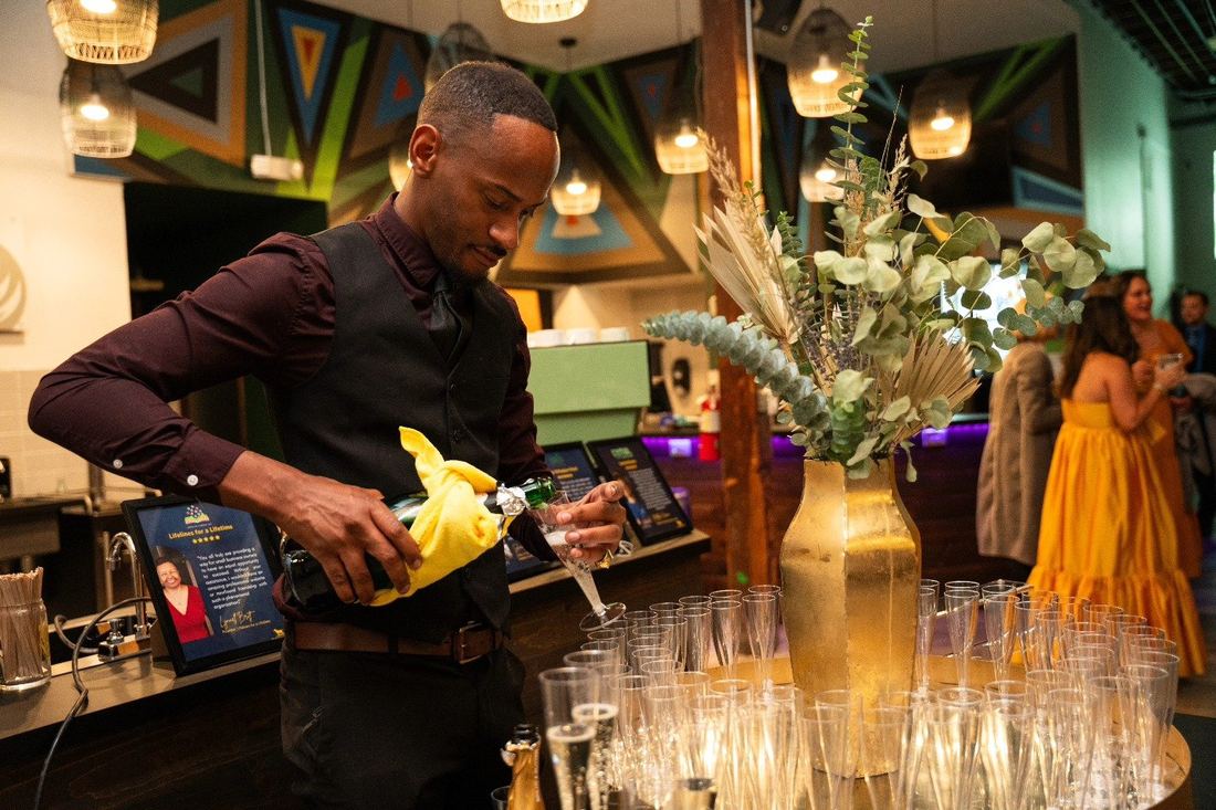 A server pouring champagne into rows of flutes at the 3rd Annual Fall Ball